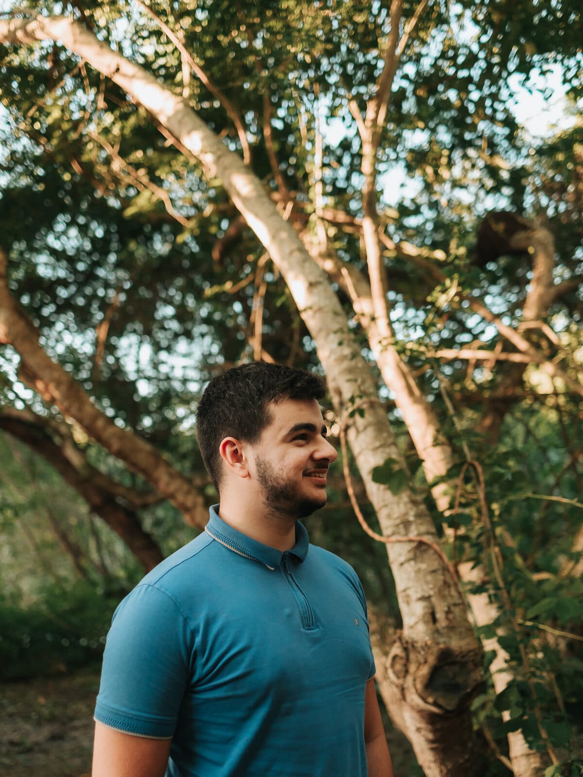 Arthur sorrindo entre as árvores, no fim da tarde